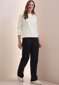 Felpa bianca con un design grafico testurizzato, abbinata a pantaloni neri e sneaker bianche. Tessuto morbido, vestibilità rilassata e maniche 3/4.