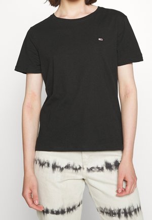 Person wearing a plain black short-sleeve t-shirt and light pants with horizontal black tie-dye stripes near the knees.