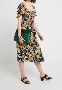 Kwiatowa midi sukienka z krótkimi bufkami, na czarnym tle, w kolorowe wzory liści i kwiatów. Połącz ją z zieloną torebką i czarnymi sandałami na słupku.