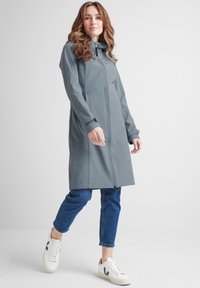 Light grey waterproof coat with a zip front, hood, and side pockets, paired with blue jeans and white sneakers. Smooth texture and modern design.