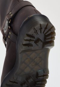 Brown leather boot with sturdy black rubber sole. Features include textured grip pattern and metal buckle accents.