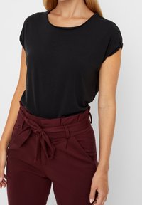 Haut noir à manches courtes associé à un pantalon bordeaux taille haute avec ceinture nouée et poches latérales, en tissu lisse.