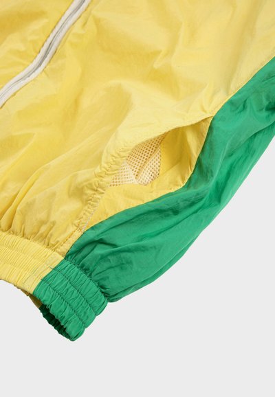 Manche de coupe-vent jaune et verte avec poignet élastique et ventilation en maille sous le bras.