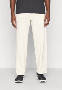 Calças brancas de corte descontraído, texturizadas com um padrão de grelha subtil, combinadas com sapatilhas pretas. Adequadas para uso casual.