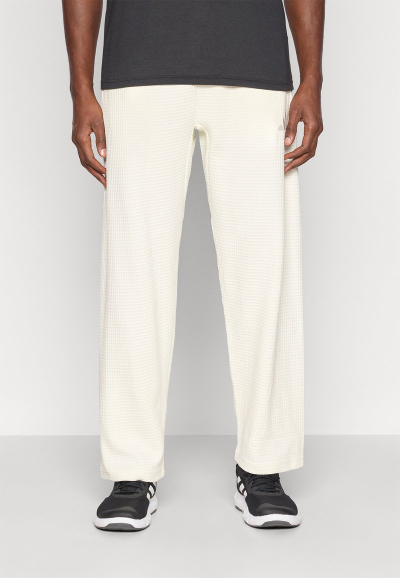 Calças brancas de corte descontraído, texturizadas com um padrão de grelha subtil, combinadas com sapatilhas pretas. Adequadas para uso casual.