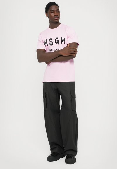 Rosa bomuld T-shirt med sort "MSGM MILANO" tekst, parret med sorte cargo bukser med sidelommer og løs pasform.