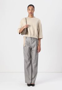 Felpa beige a maniche lunghe, con orlo elastico, abbinata a pantaloni a quadri grigi a vita alta e scarpe nere slip-on. Borsa mini in mano.