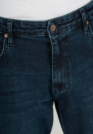 Jeans de mezclilla azul oscuro con corte recto, cierre de botón de cobre y un leve efecto de desgaste en la parte delantera. Diseño clásico de cinco bolsillos.