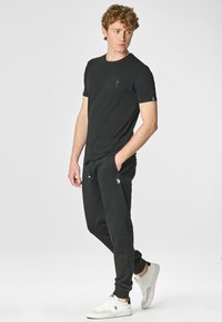 T-shirt nera in cotone con un logo discreto, abbinata a pantaloni jogger neri con tasche laterali e sneaker bianche con accenti neri.