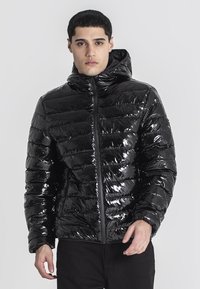 Giacca a vento nera con finitura lucida, cappuccio e chiusura frontale con zip; presenta un design trapuntato orizzontale e polsini elasticizzati.