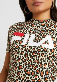 Camisa de manga corta de estampado de leopardo en color beige, con manchas negras y naranjas. Presenta un logo blanco de "FILA" de forma prominente en el pecho.