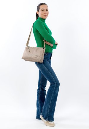 Beige fabric handbag with a textured surface and printed logo, carried by a person wearing a green ribbed sweater and flared jeans.