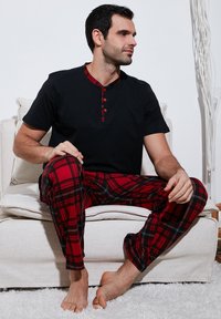 Mannen pyjama set met een zwart overhemd met korte mouwen en een rood geruit kraag, en rode geruite broek met zwart-witte accenten.
