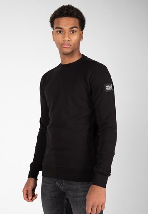 Sudadera negra de manga larga hecha de una mezcla de algodón. Presenta puños y dobladillo acanalados, con un parche de logo en la manga izquierda.