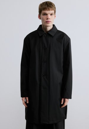 Μαύρο μακρύ παλτό από λείο ύφασμα, με γιακά, έξι κουμπιά στο μπροστινό μέρος και ευθεία σιλουέτα με πλαϊνές ραφές.