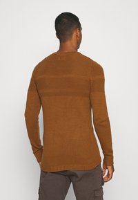 Brązowy sweter dziergany z prążkowaną strukturą, dopasowany krój i długie rękawy. Szew biegnący przez ramiona i plecy, z okrągłym dekoltem.