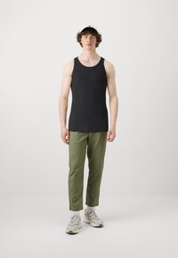 Černé žebrované tílko v kombinaci s olivově zelenými zúženými kalhotami a krémovými teniskami. Modelka předvádí ležérní venkovní outfit. Na hlavě má bílou čepici.