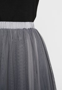Grijze tule rok met een geplooide elastische tailleband. De stof heeft een doorschijnende, gelaagde textuur die een volumineuze uitstraling creëert.