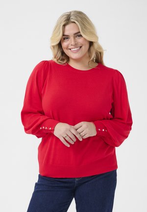 Red knit sweater featuring long puff sleeves with button details at the cuffs, a round neckline, and a relaxed fit. Worn over dark denim.