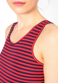 Punainen ja laivastonsininen raidallinen ilmanhiha-toppi, jossa on pyöreä pääntie. Ominaisuuksiin kuuluu pehmeä, joustava kangas ja näkyvät saumat reunoilla.