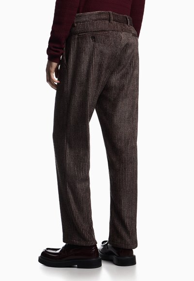 Pantaloni marroni a righe con una vestibilità ampia, caratterizzati da un design plissettato, tasche posteriori e un tessuto testurizzato, abbinati a scarpe lucide.