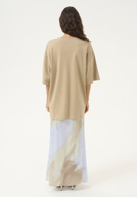 Beige Oversize-T-Shirt mit lockeren kurzen Ärmeln, kombiniert mit einem langen, fließenden Rock im Aquarellmuster in Hellblau und Beige.