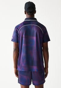 Αθλητικό πουκάμισο με μοτίβα σε μωβ και μπλε, με κοντά μανίκια, γιακά και λευκές λεπτομέρειες, συνδυασμένο με αντίστοιχο σορτς.