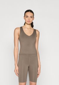 Débardeur marron extensible avec un col en v et de larges bretelles, associé à un short de vélo assorti, les deux présentant une texture lisse et mate.