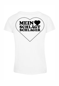Bílá bavlněná tričko s černým srdcem a textem "MEIN ♥ SCHLÄGT SCHLAGER" v tučném písmu na zadní straně.