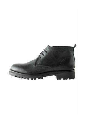 Bottine en cuir noir avec une finition lisse, bout arrondi, laçage à six œillets, et une semelle en caoutchouc robuste avec un motif détaillé.