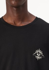 Black t-shirt with a crew neck, featuring a white eye graphic surrounded by sunburst details on the chest. Smooth cotton texture.
