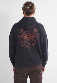 Hoodie noir avec cordon de serrage, présentant un design graphique circulaire orange et violet au dos. Le tissu semble doux et décontracté.