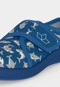Chausson bleu pour enfants avec motifs de requin gris et bride Velcro réglable sur fond blanc.