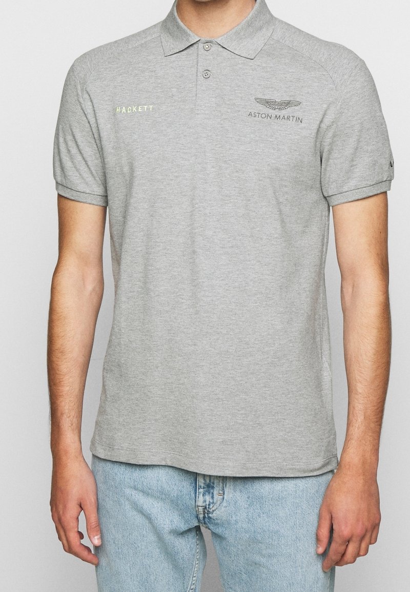 Šedé polo tričko vyrobené z bavlny, s límečkem, krátkými rukávy a vyšitými logy "HACKETT" a "ASTON MARTIN" v kontrastních barvách.
