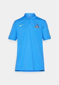 Blå Nike polo shirt med gul swoosh, Tottenham Hotspur emblem på brystet og logo på højre ærme, vist på hvid baggrund.