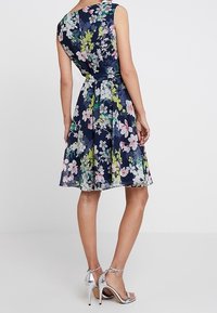 Blåblommig klänning med ärmlös design, åtsittande midja och svängande kjol. Har färgglada blommor och en lätt textur.