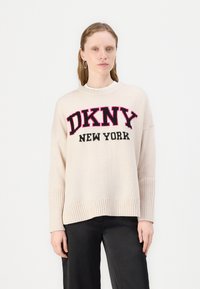 Suéter tricotado de cor creme com punhos e barra canelados, apresentando um ousado texto preto e rosa "DKNY NEW YORK" na parte da frente.