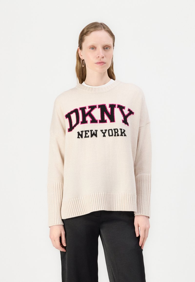 Suéter tricotado de cor creme com punhos e barra canelados, apresentando um ousado texto preto e rosa "DKNY NEW YORK" na parte da frente.