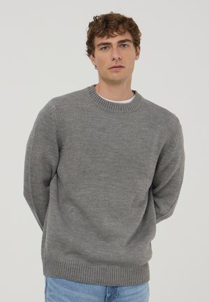 Maglione grigio lavorato a maglia con collo a giro, polsini e orlo a coste, con una finitura testurizzata. Indossato con jeans azzurri chiari.