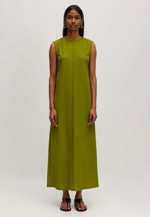 Groene mouwloze maxi-jurk, gemaakt van een gladde stof, heeft een rechte snit, is enkel-lang en heeft subtiele detaillering van voornaad. Platte zwarte sandalen.