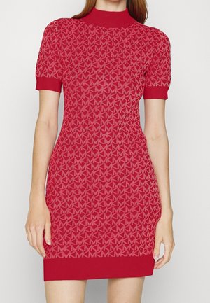 Frau trägt ein rotes Strickkleid mit kurzen Ärmeln, wiederkehrendem geometrischem Muster und geripptem Ausschnitt, Bündchen und Saum.