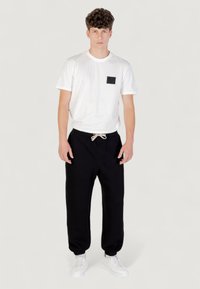 Witte katoenen t-shirt met een zwarte vierkante zak, gecombineerd met zwarte sweatpants met een verstelbare trekkoord en witte sneakers.