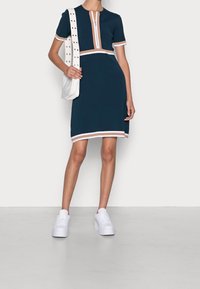 Robe à manches courtes bleu marine avec col zippé, rayures beige et blanches, associée à des baskets à plateforme blanches et un sac bandoulière blanc.