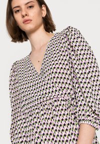 Vestido estampado com decote em V, mangas bufantes e um laço na cintura. O tecido é leve e apresenta um design geométrico nas cores rosa, verde e preto.