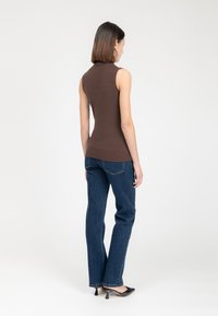 Top senza maniche in maglia marrone con colletto alto, abbinato a jeans dritti blu scuro e scarpe con tacco nere. Design minimalista.