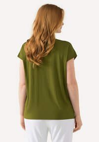 Olivově zelená blůza s krátkými rukávy, volný střih a hladká textura. Má kulatý výstřih a sahá do poloviny boků.