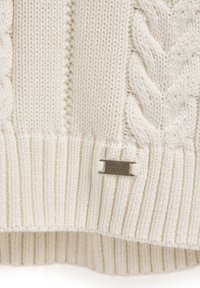 Garnett i kabelstickning i off-white, med ribbad nederkant och muddar. Metallmärke "Polo Club" längst ner till höger ger en detalj.