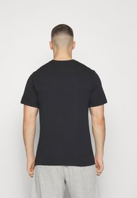 Musthave musta lühikeste varrukatega T-särk, mis on valmistatud puuvillast, ümarate kaelustega ja vähese lõikega. Seljaosa on sujuva, mustritevaba kangaga.