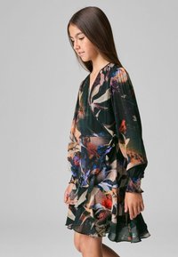 Blommigt tryckklänning med långa puffärmar, djup V-ringning och volangdetaljer. Designen inbegriper mörka färger med livliga blommönster.