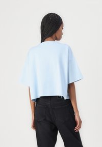 Ljusblå bomulls crop top med korta ärmar och avslappnad passform, kombinerad med svarta högmidjade jeans med bakfickor.